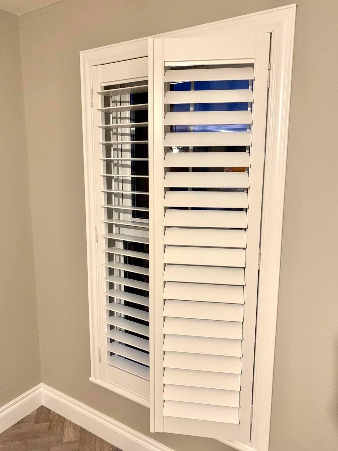 A pair of white shutters on a window in a room.