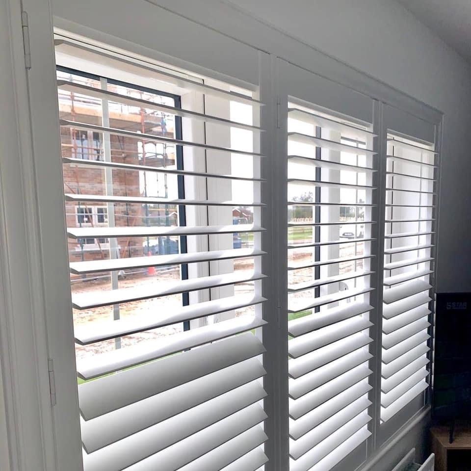 A window with white shutters on it and a building in the background