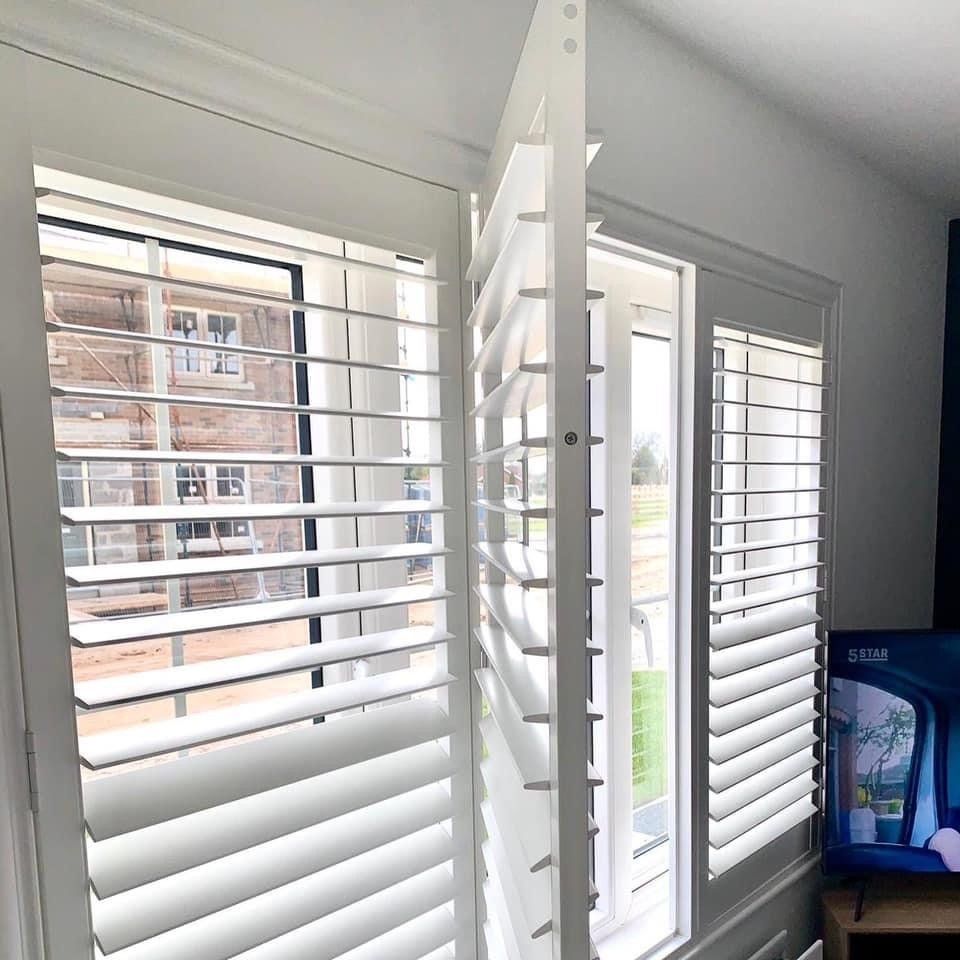 A living room with white shutters on the windows and a television.