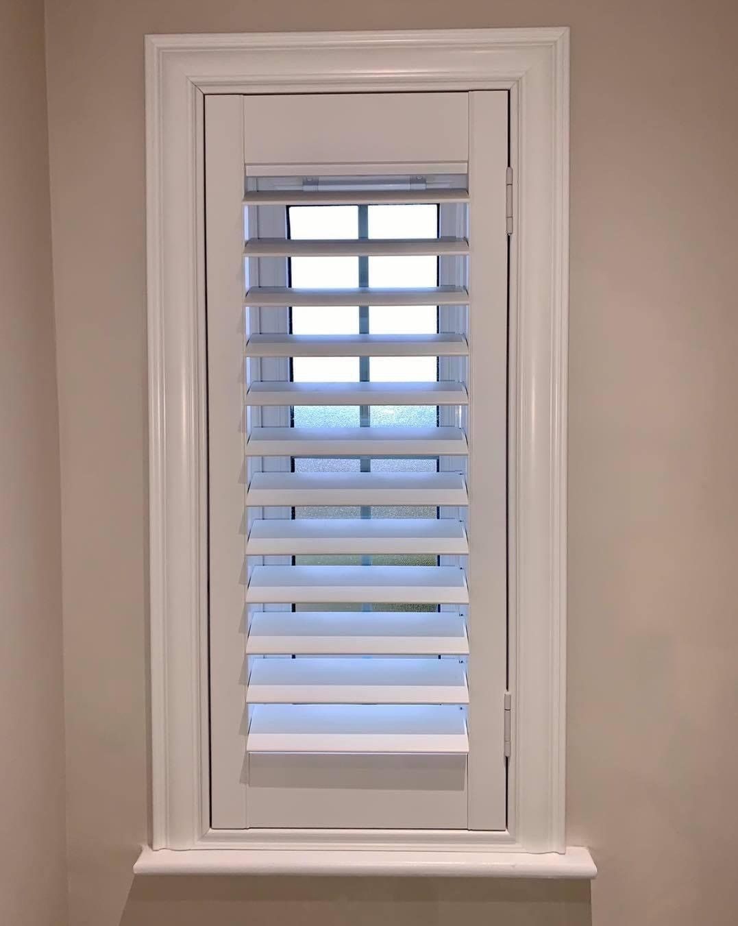 A window with white shutters on it in a room.