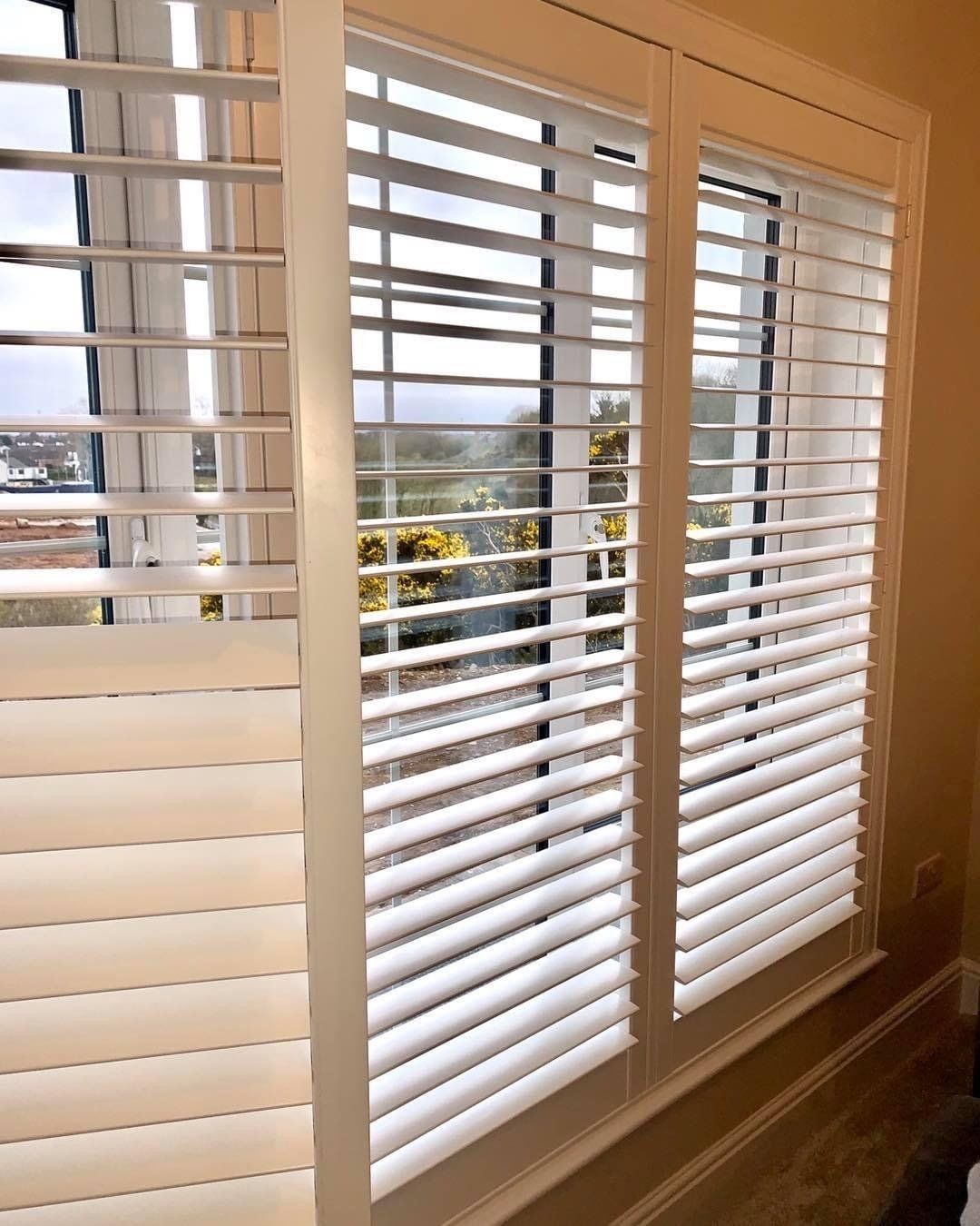 A pair of white shutters on a window in a room.