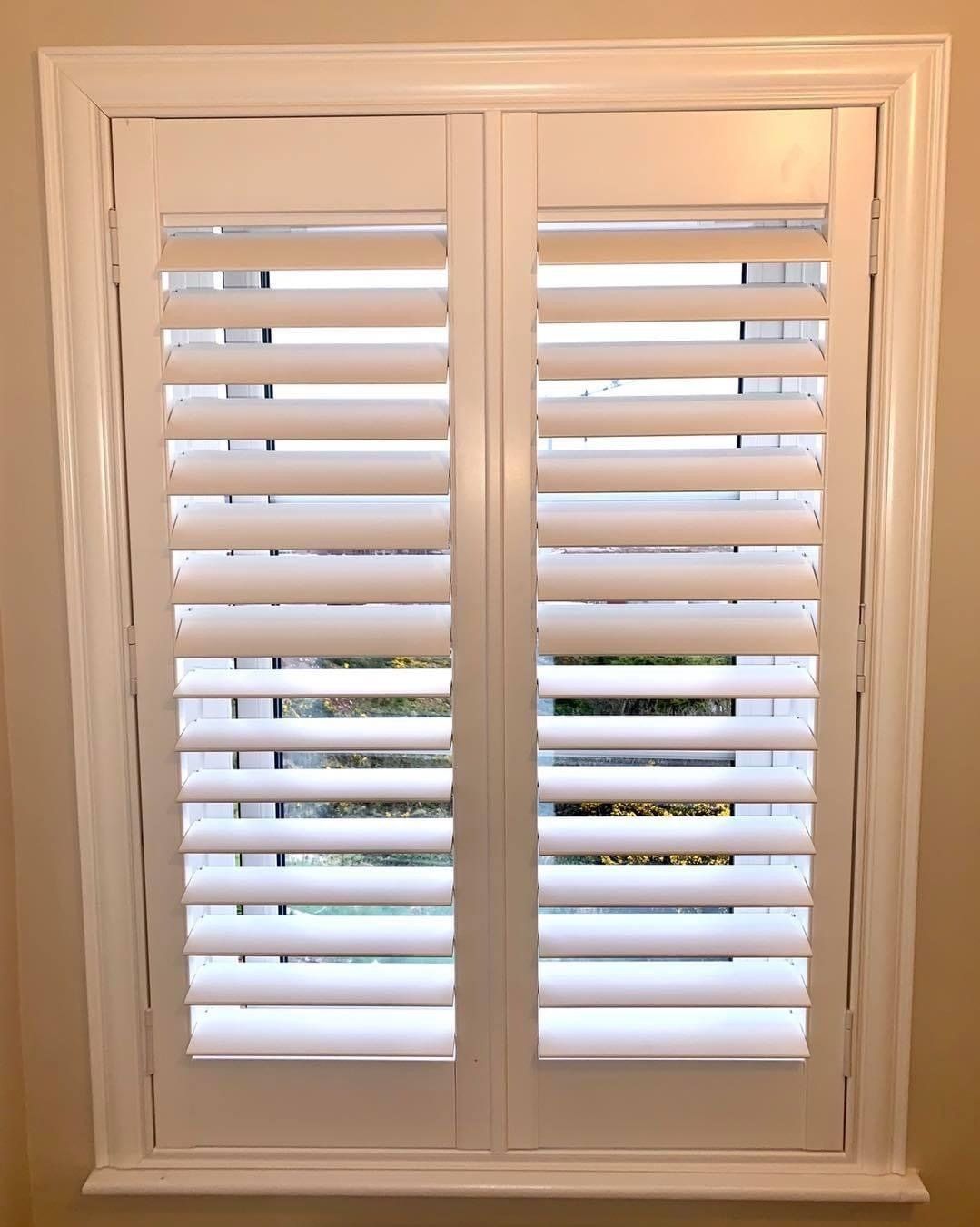 A window with white shutters on it in a room.