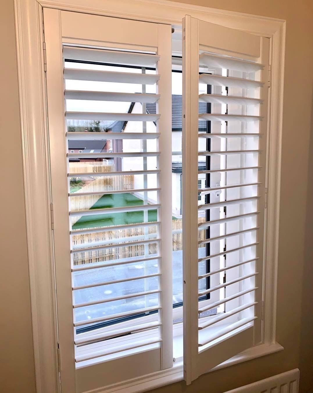 A window with white shutters on it and a view of a yard.