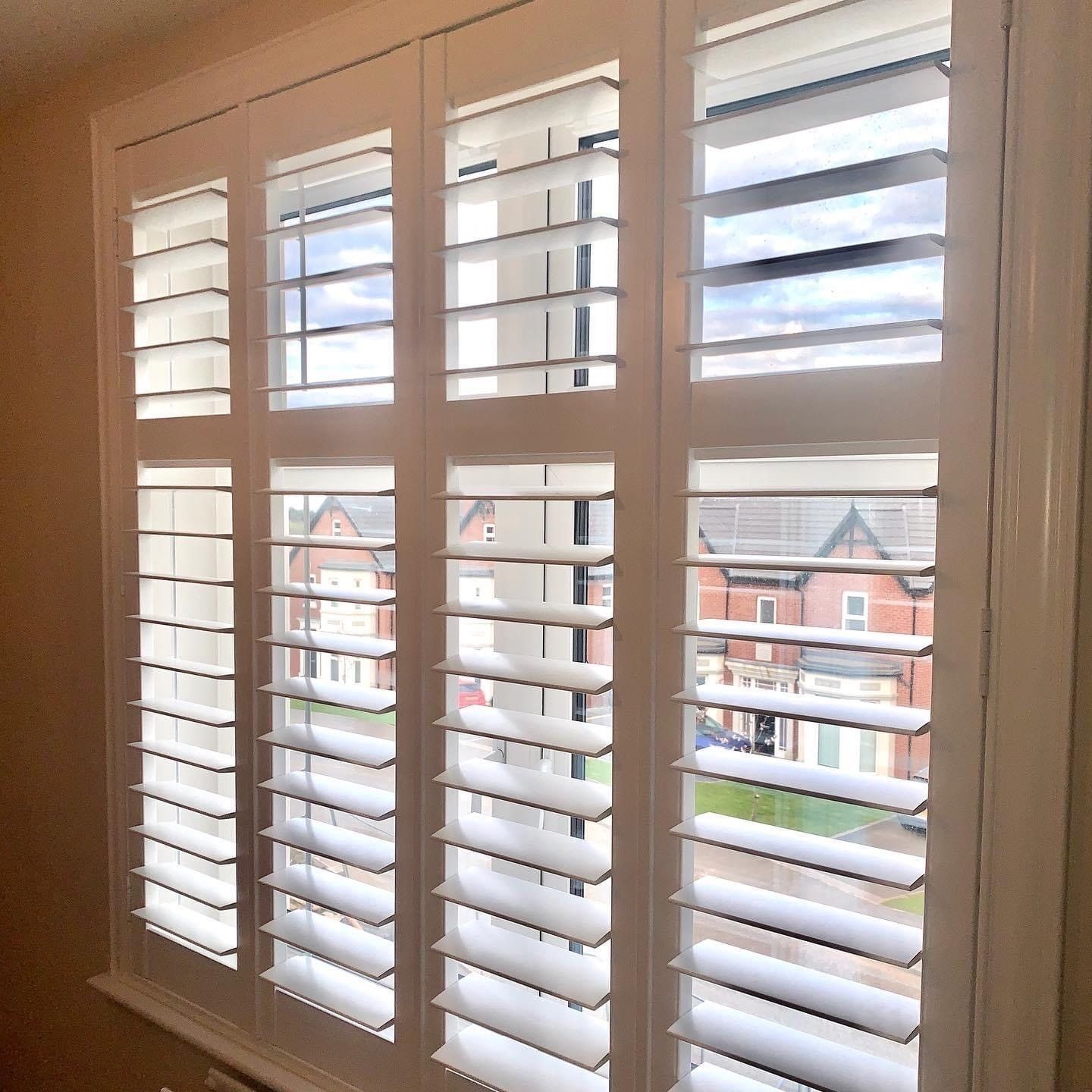 A window with white shutters on it and a view of a house.