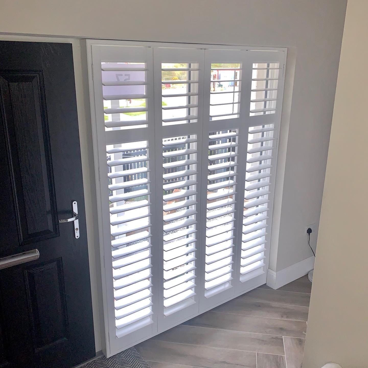 A room with a black door and white shutters on the window.