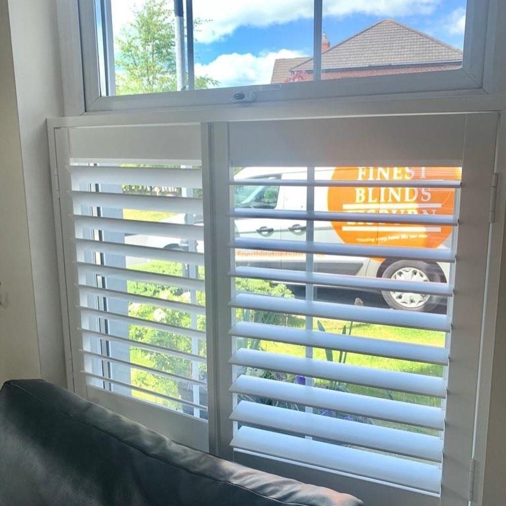 A blinds van is parked in front of a window with shutters.