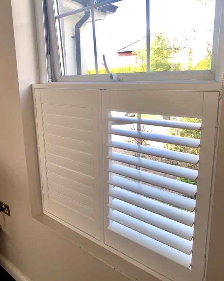 A window with white shutters on it in a room.
