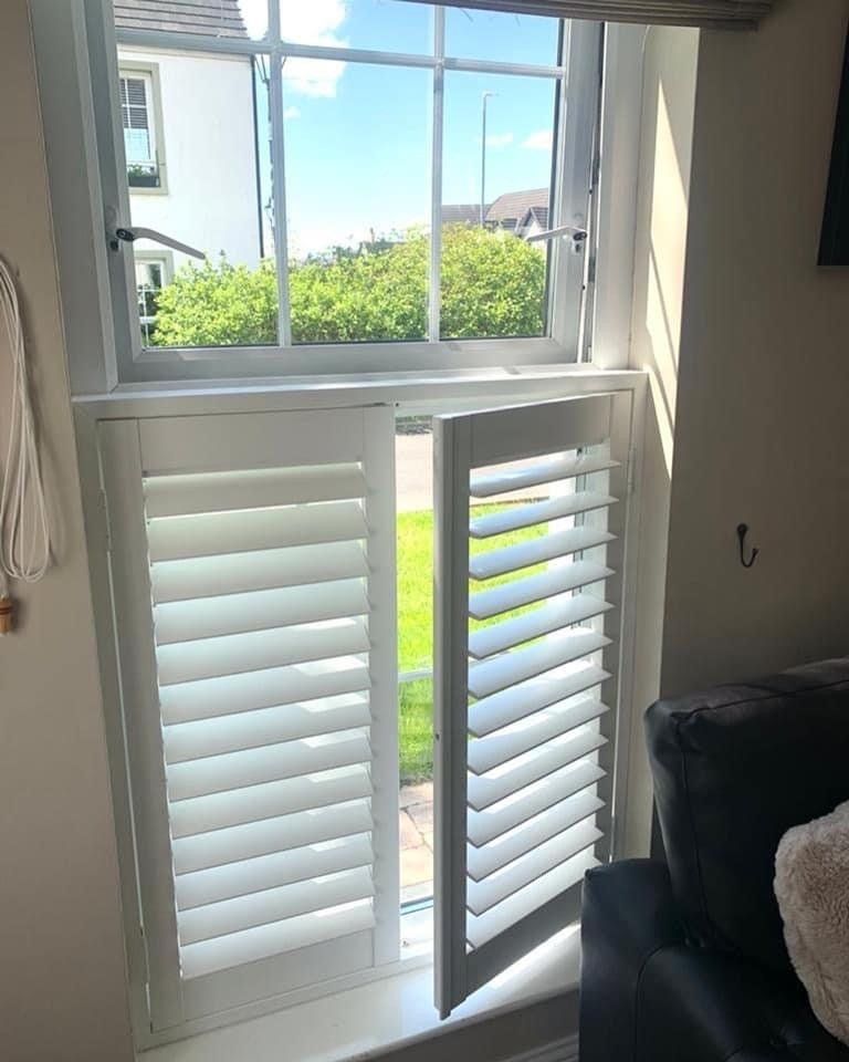 A living room with a couch and a window with shutters open.