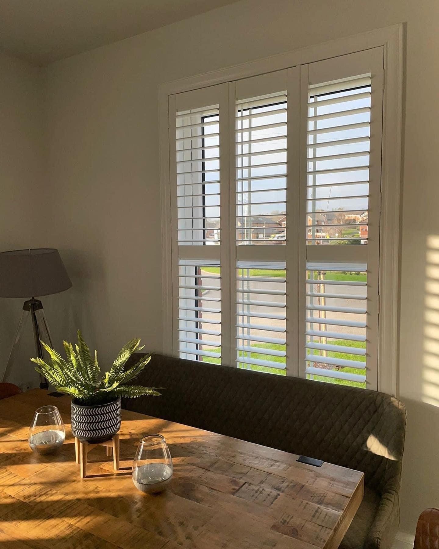 A dining room table with a plant on it and shutters on the windows.