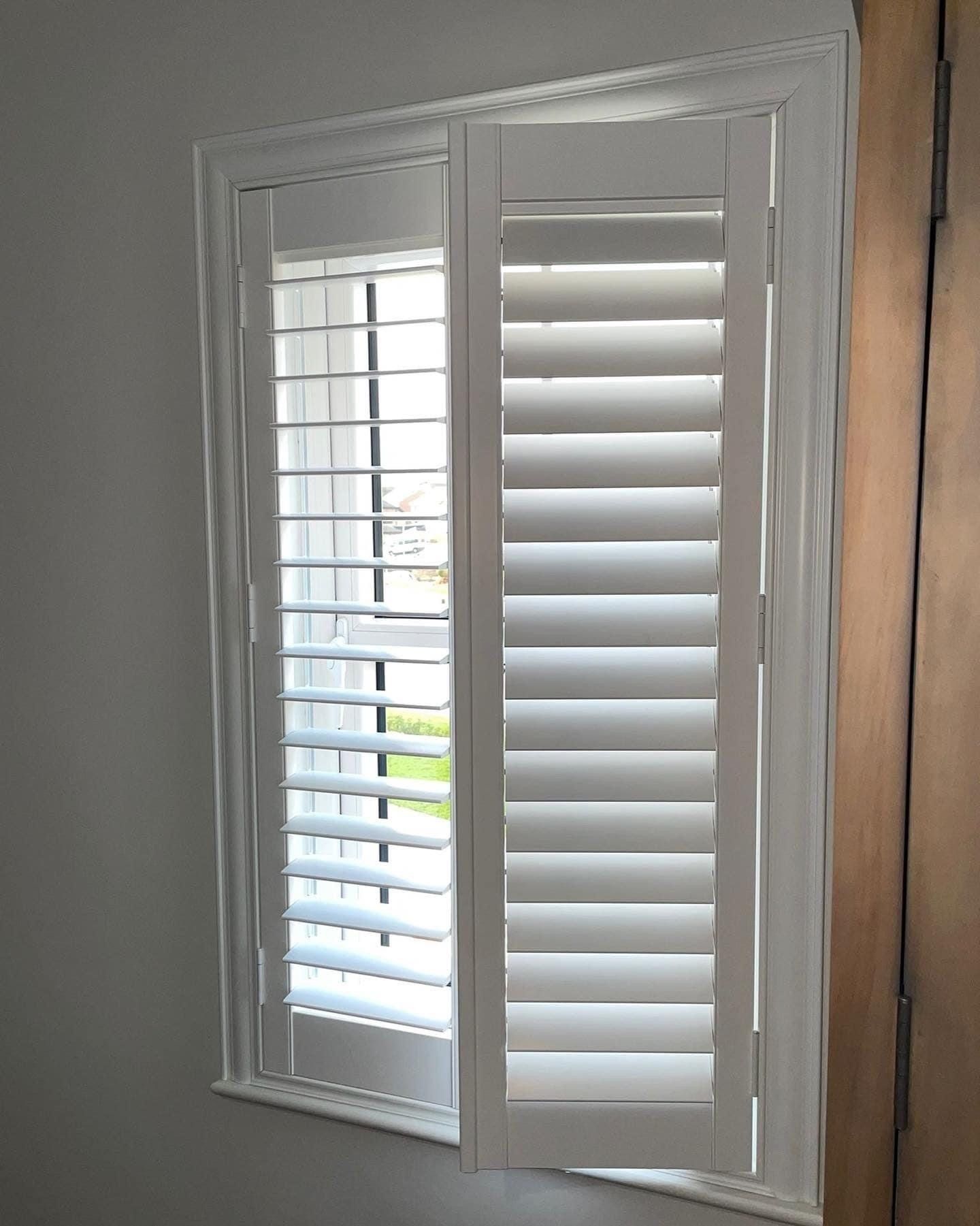 A window with white shutters on it in a room.