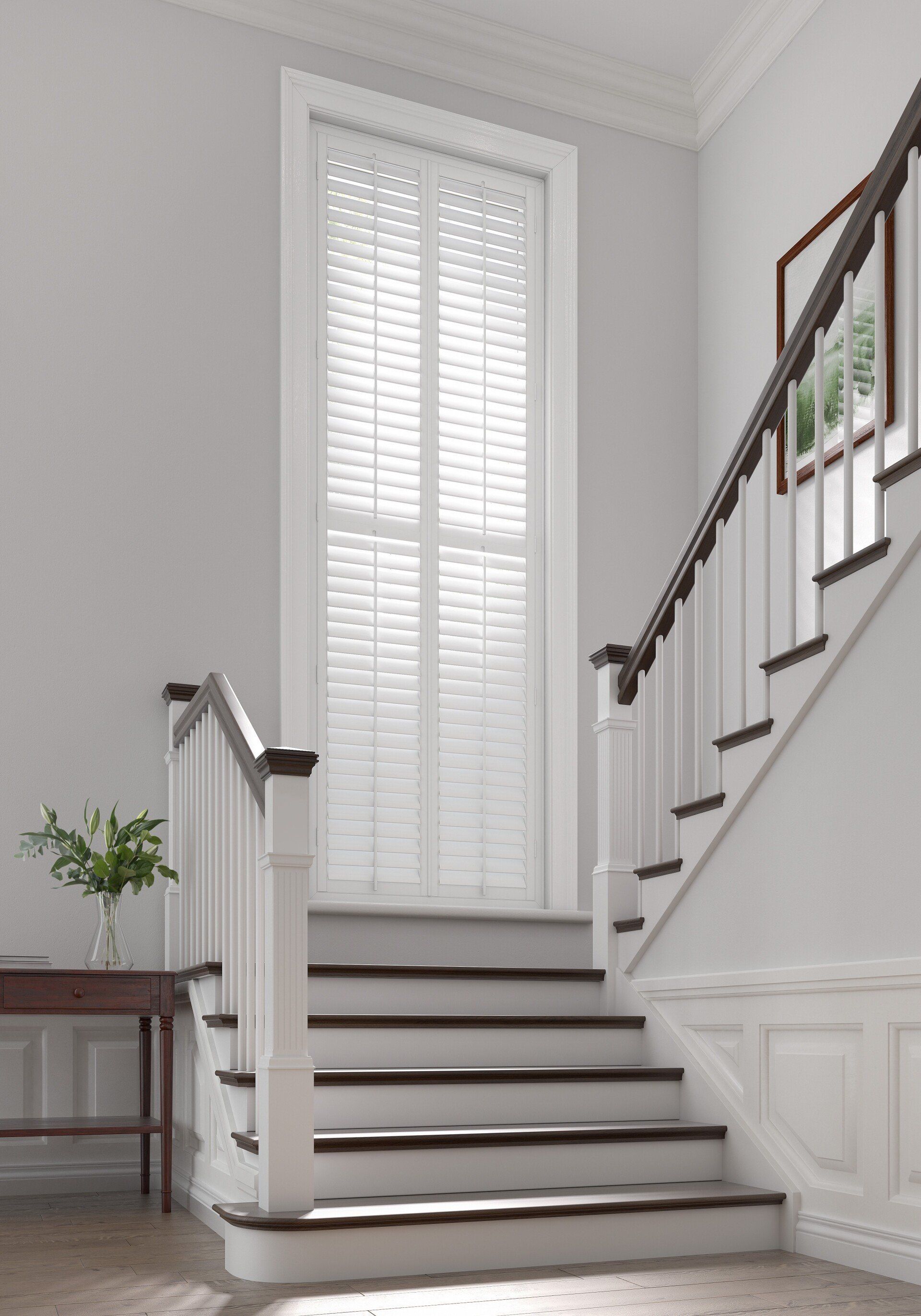 A white staircase with a wooden railing and shutters in a hallway.