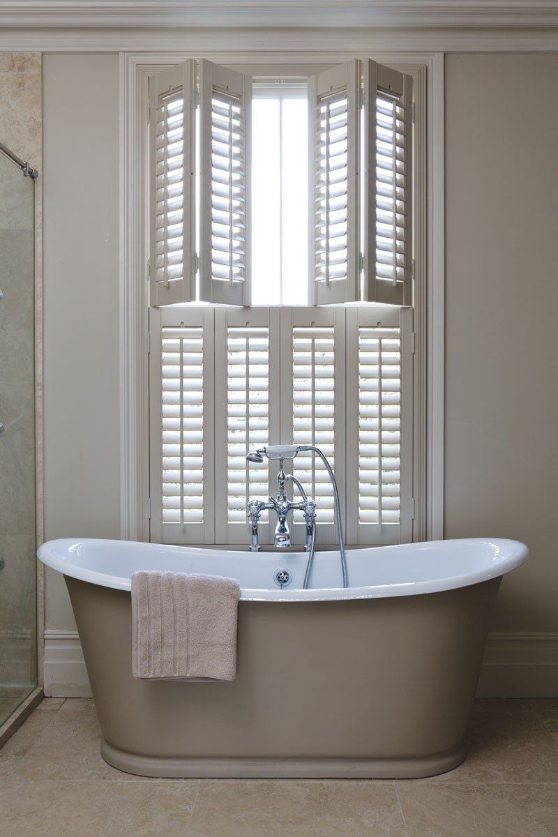 A bathtub in a bathroom with shutters on the window