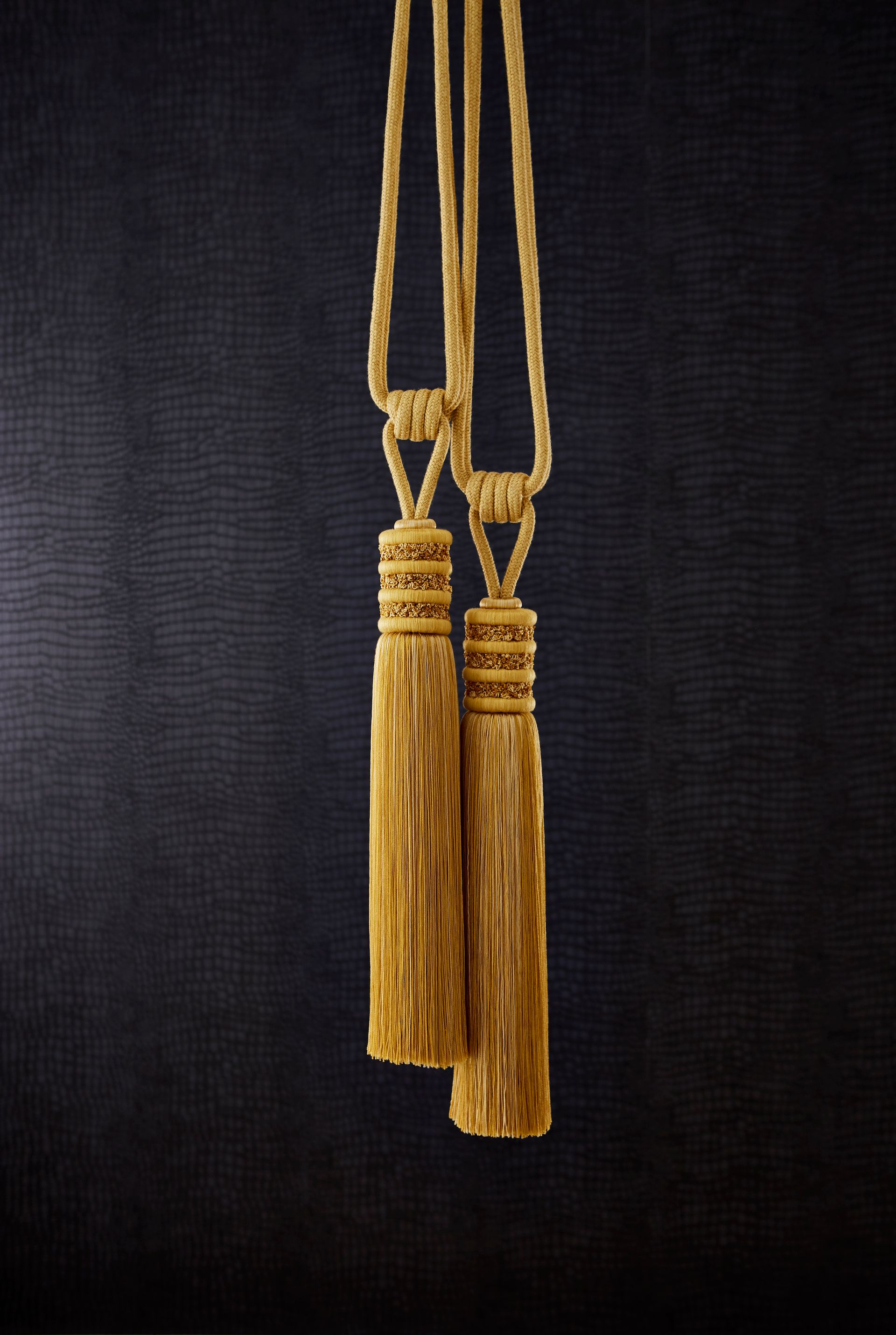 Two gold tassels hanging from a rope on a black background