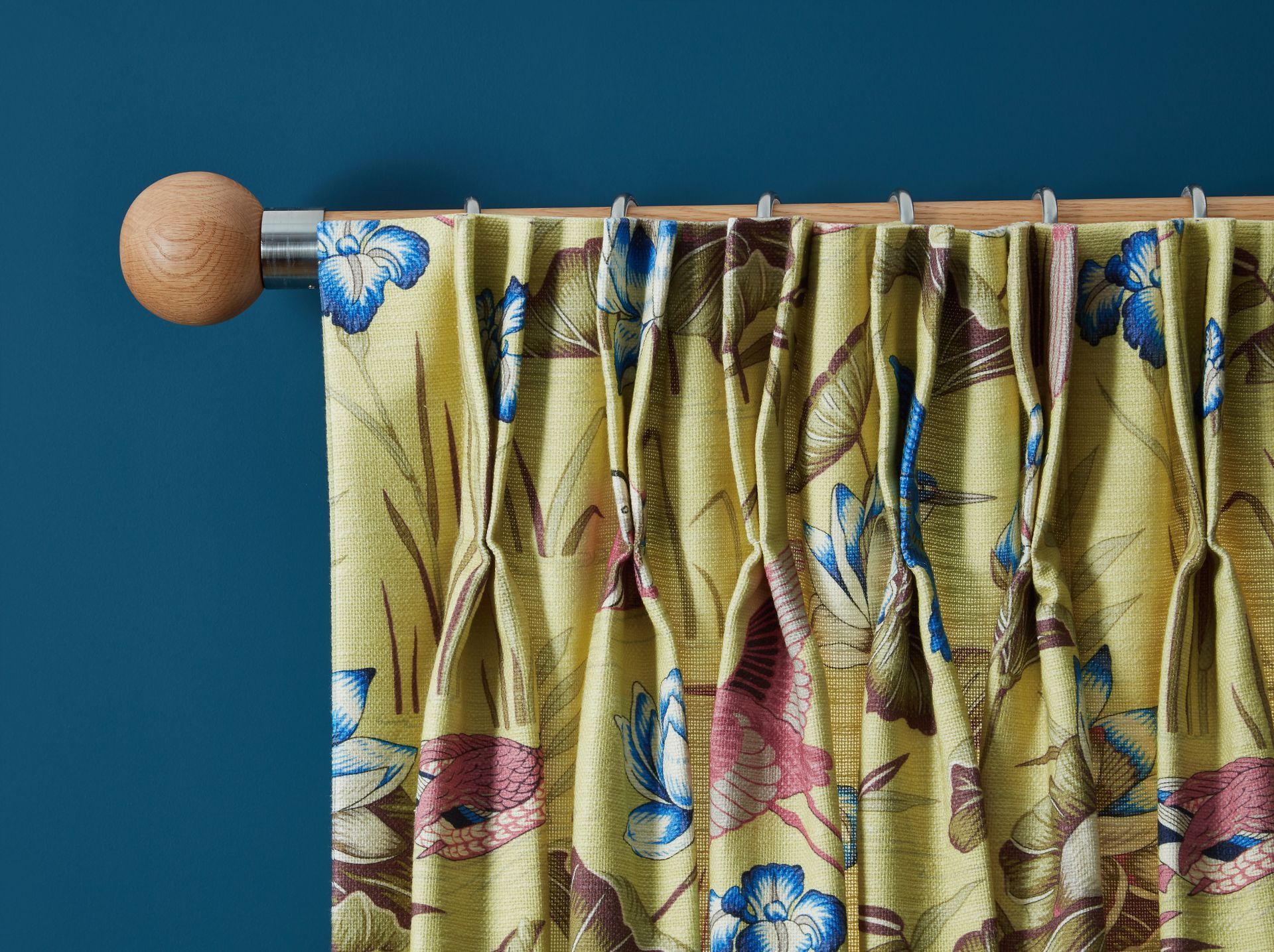 A yellow curtain with flowers on it is hanging on a wooden pole against a blue wall.