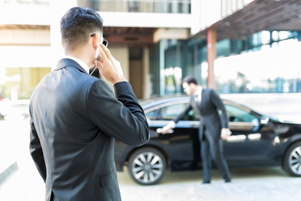 A Man In A Suit Is Talking On A Cell Phone In Front Of A Car — Coastal Protection Services Pty Ltd In Wyong, NSW