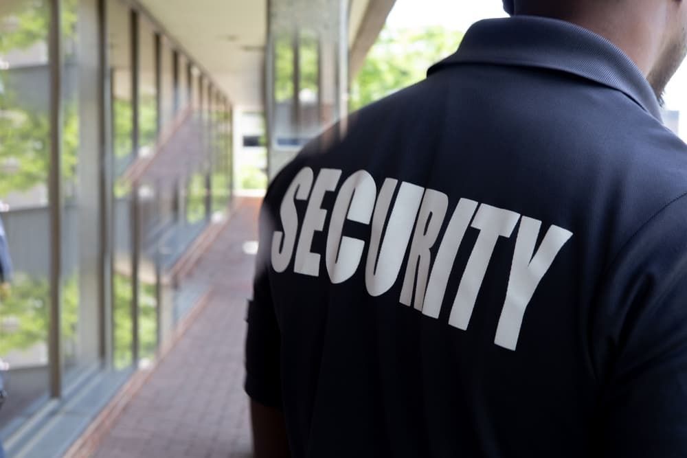 A Man Wearing A Black Security Shirt Is Walking Down A Hallway — Coastal Protection Services Pty Ltd In Bateau Bay, NSW
