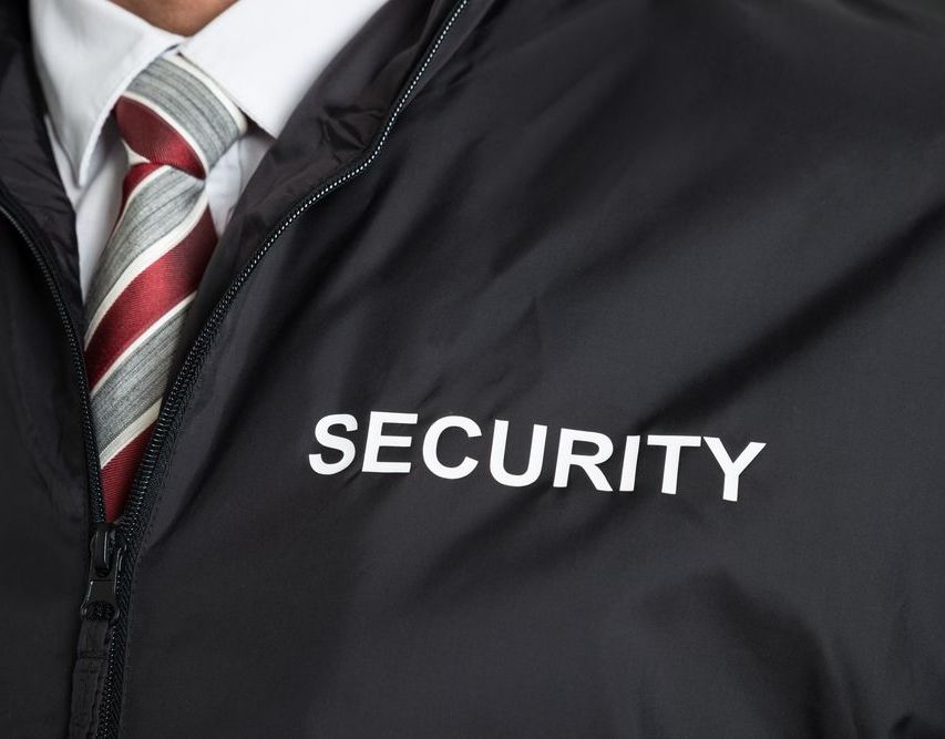 A Man In A Suit And Tie Is Wearing A Security Jacket — Coastal Protection Services Pty Ltd In Gosford, NSW