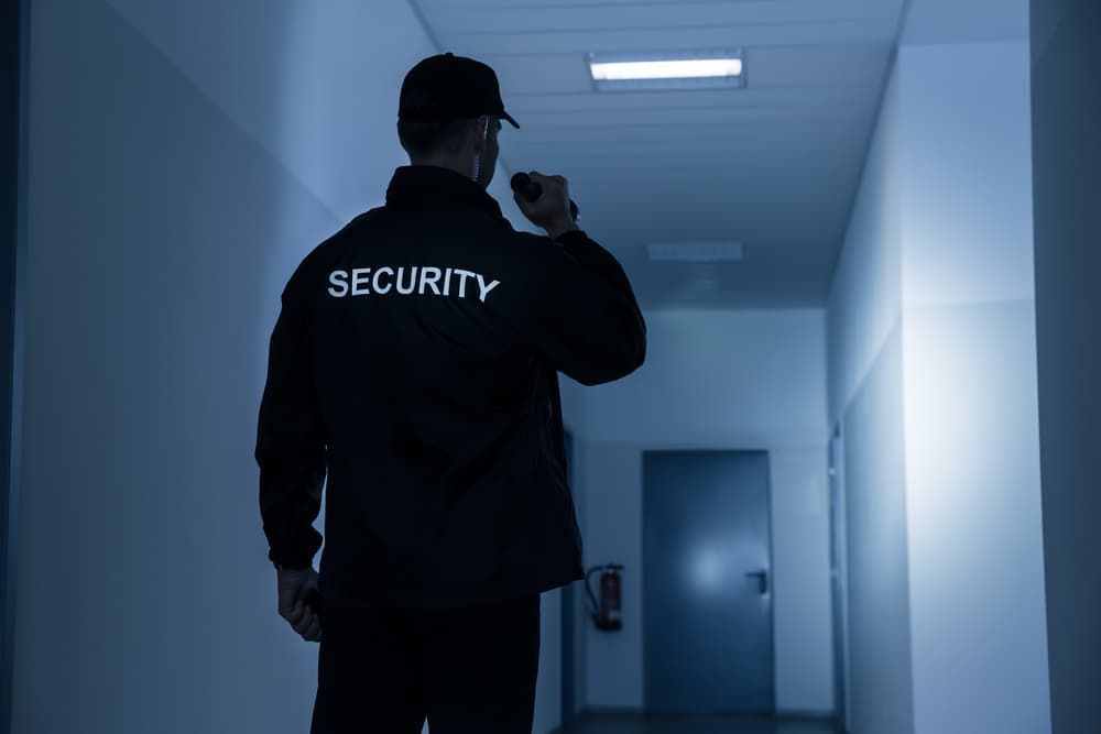 A Security Guard Is Standing In A Hallway Holding A Flashlight — Coastal Protection Services Pty Ltd In Wyoming, NSW