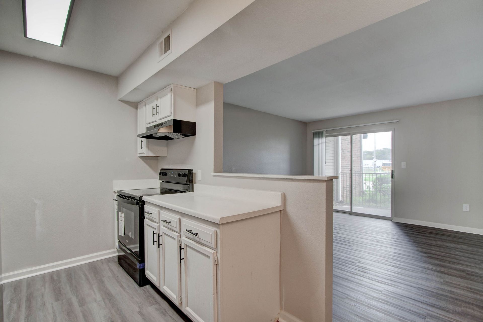 Kitchen with white cabinets, black stove, and doorway to living area with sliding glass door.