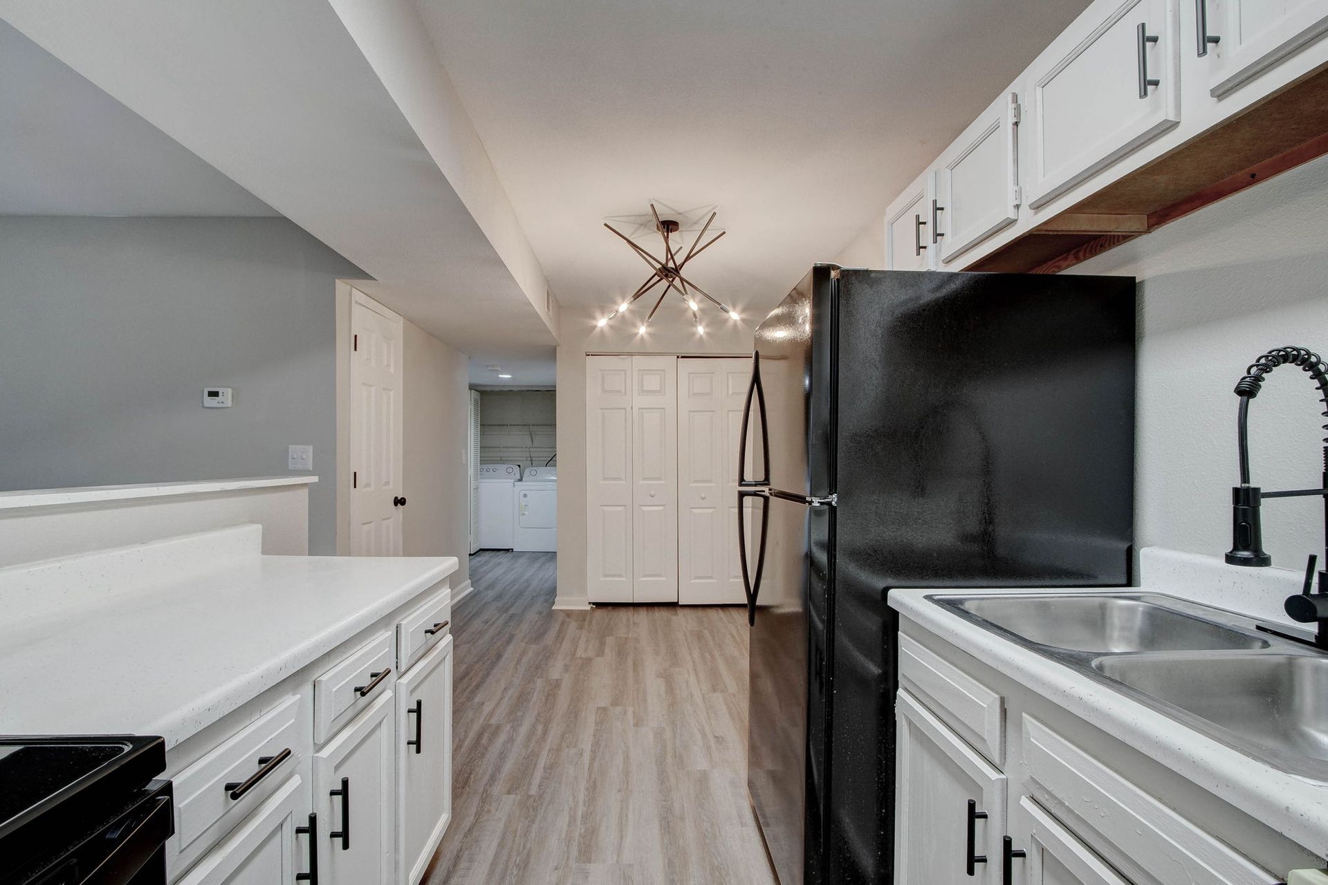 Kitchen with white cabinets, black appliances, and a view to a hallway.