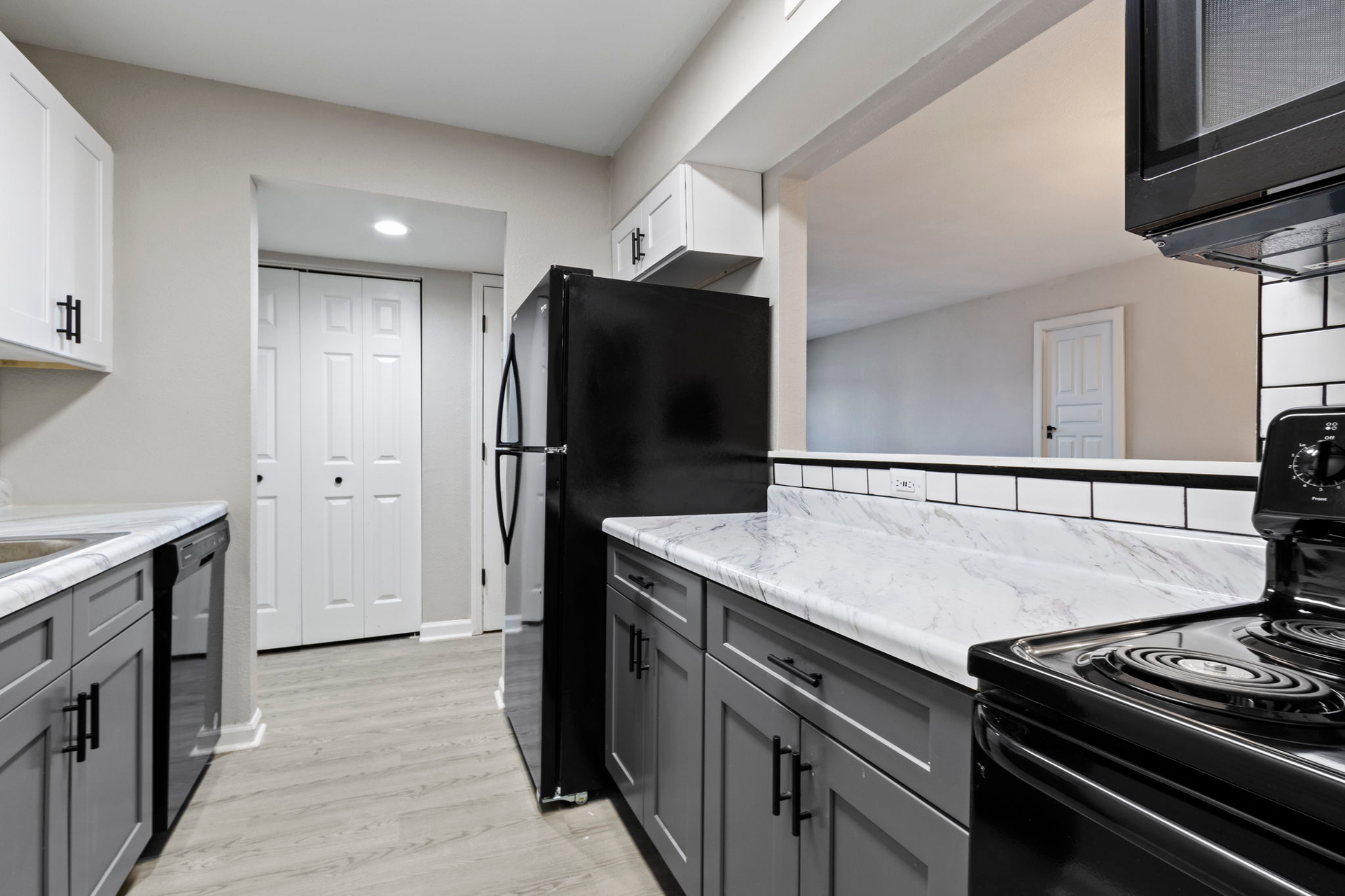 Modern kitchen with gray cabinets, white countertops, black appliances, and a view into the next room.