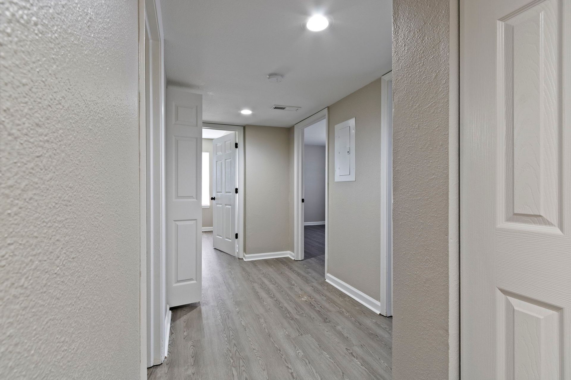 Narrow hallway with gray wood-look floor, off-white walls, and multiple doors.