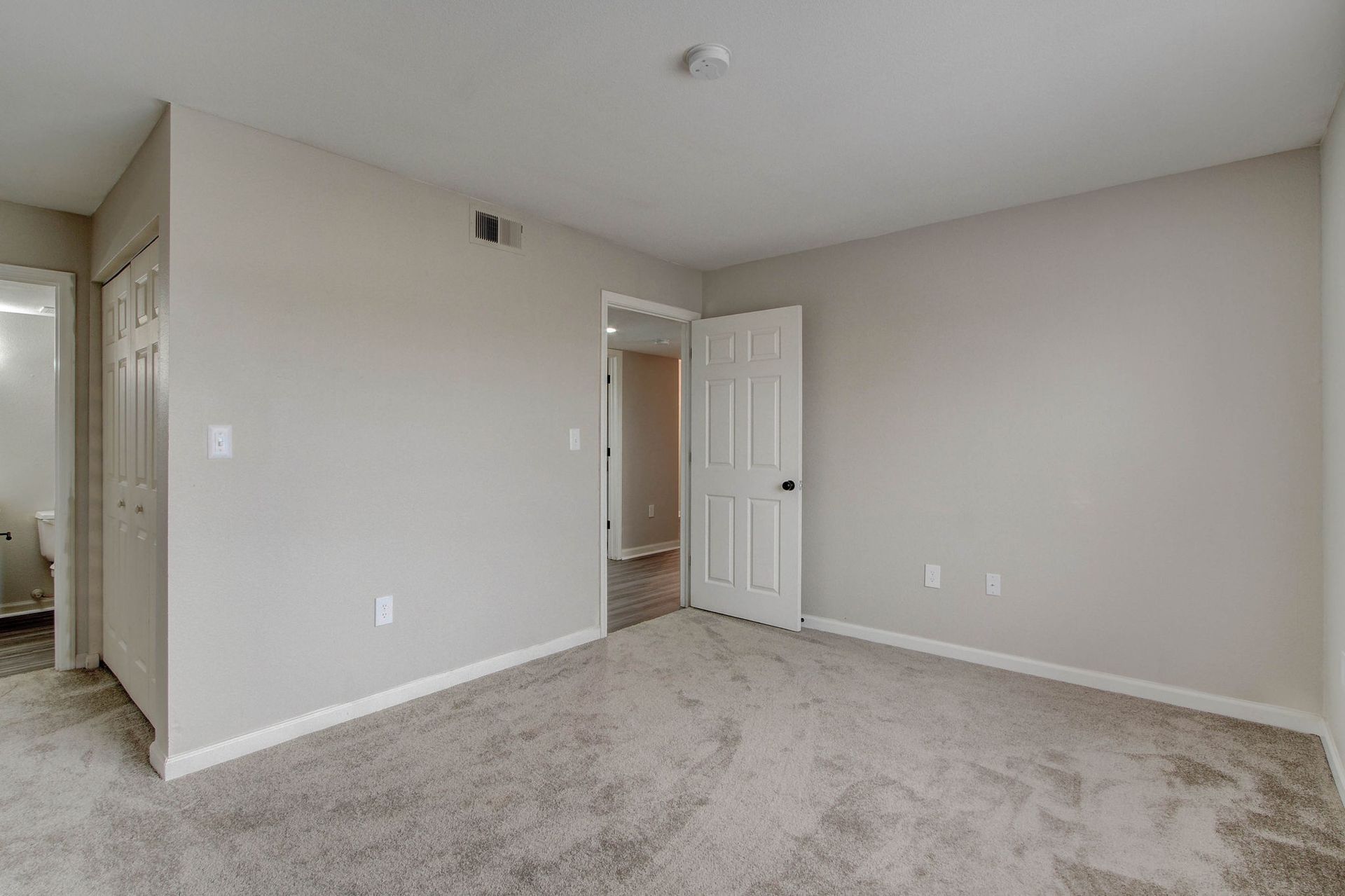 Empty bedroom with gray walls and carpet, two doorways, and a light fixture.