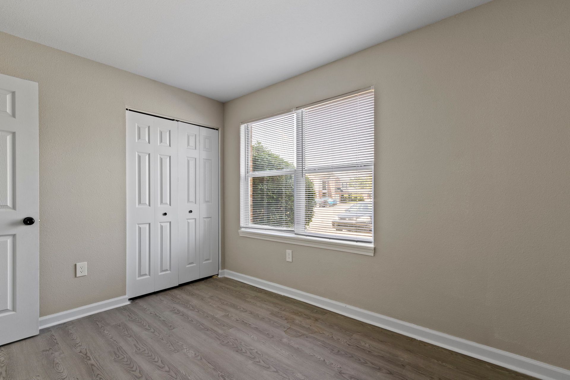Empty bedroom with closet, window, and light wood flooring.