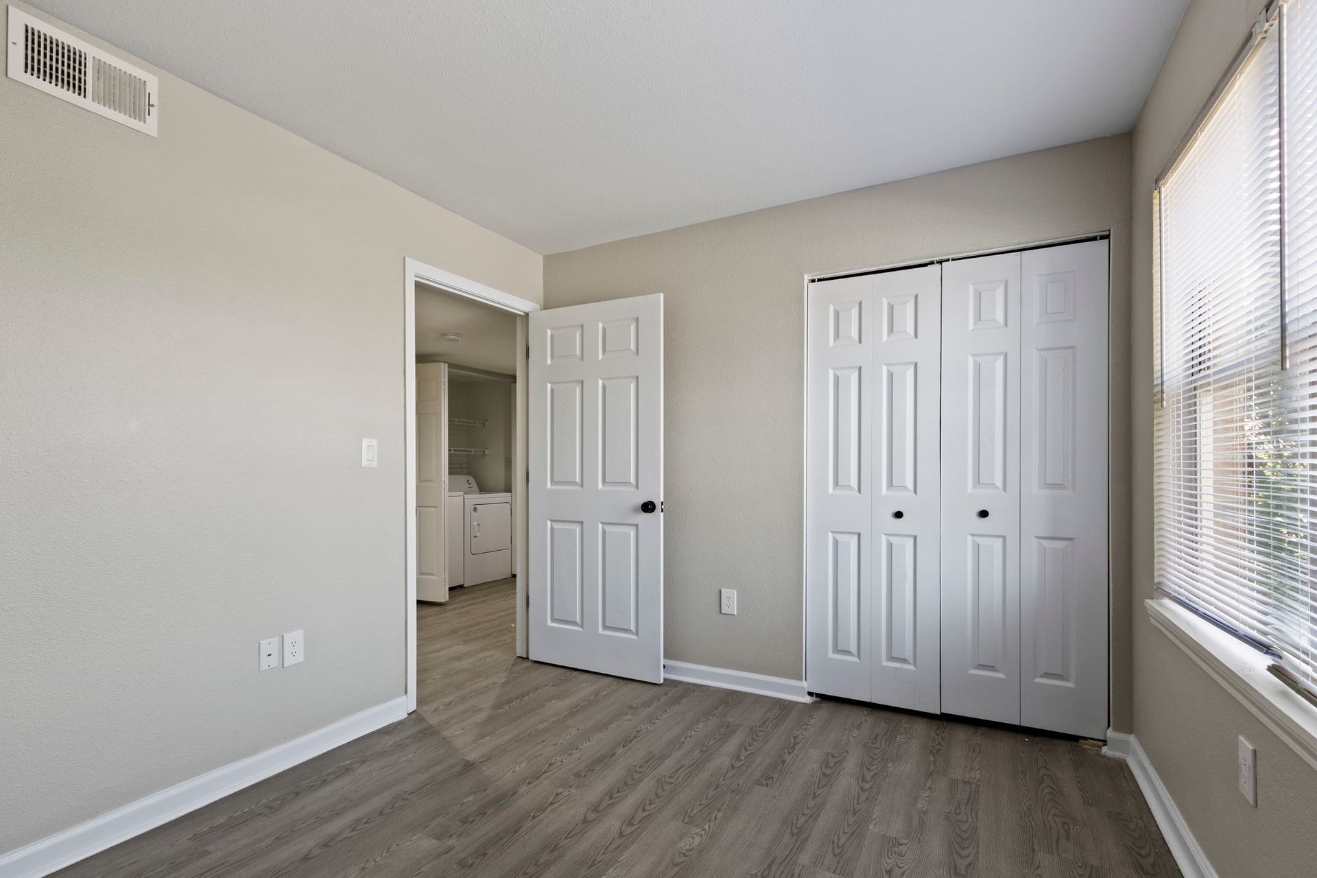 Bedroom with white doors, closet, window with blinds, and light gray walls.