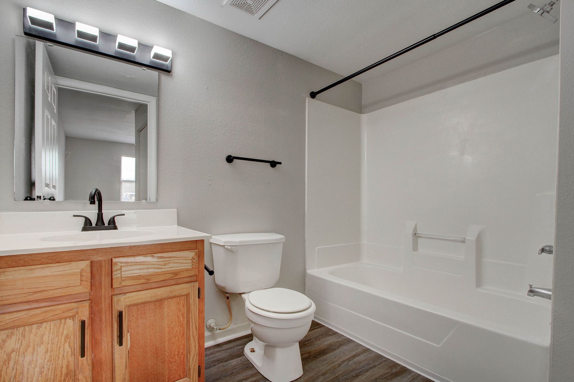 Bathroom with wood vanity, white toilet and tub, gray walls, and dark fixtures.