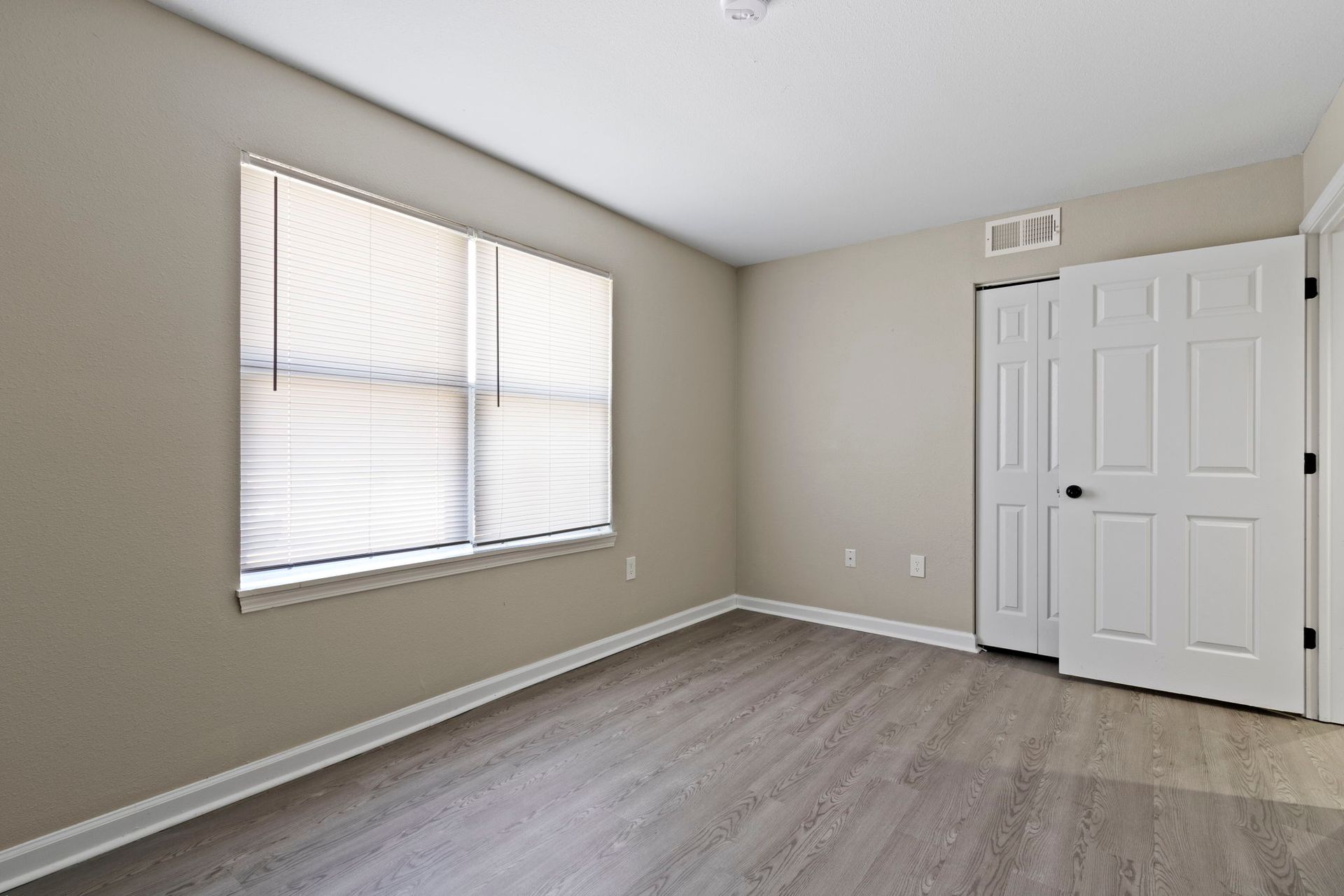Empty bedroom with grey flooring, white door, and window with blinds.
