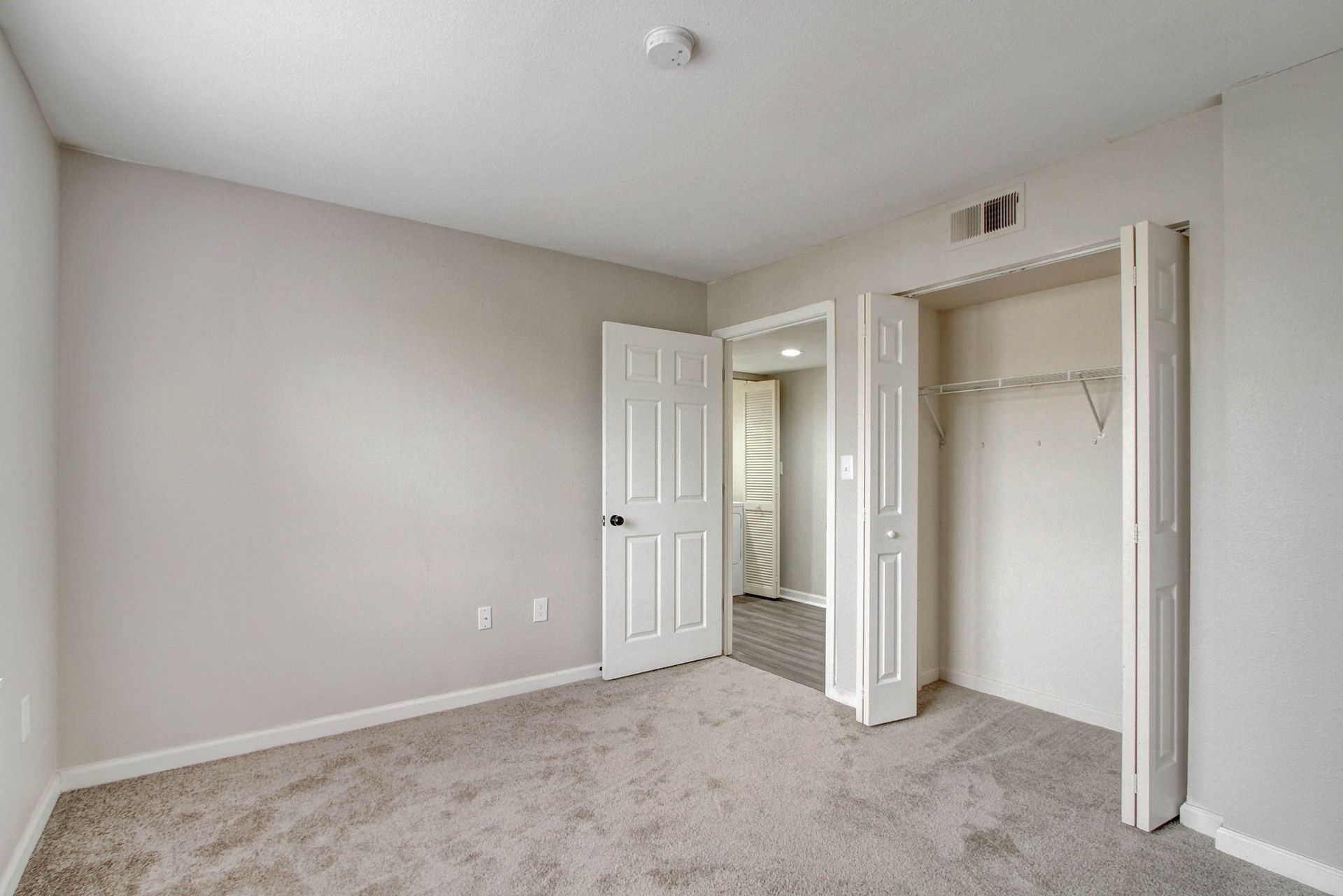 Empty bedroom with carpet, closet, and door leading to another room.