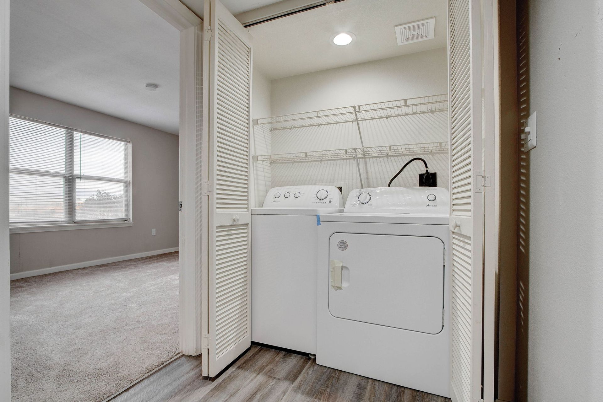 Laundry closet with a washer and dryer; room with window and carpet visible.
