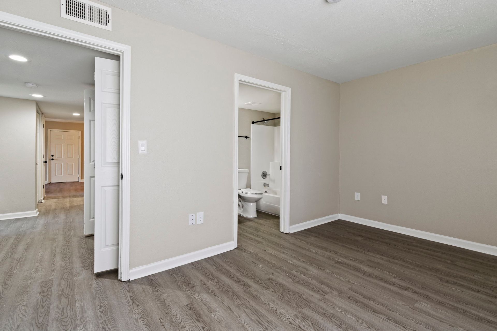 Bedroom with grey wood-look flooring, neutral walls, and white trim. Doors lead to hallway and bathroom.