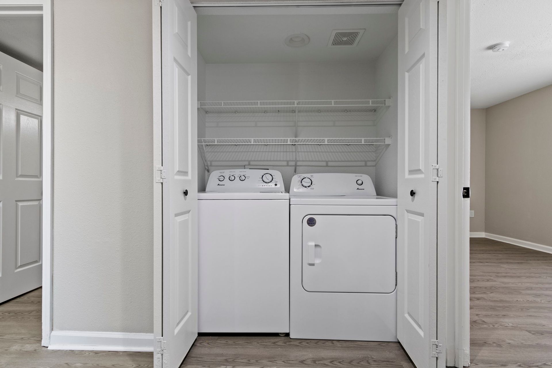 White washer and dryer inside a closet, with shelves above.