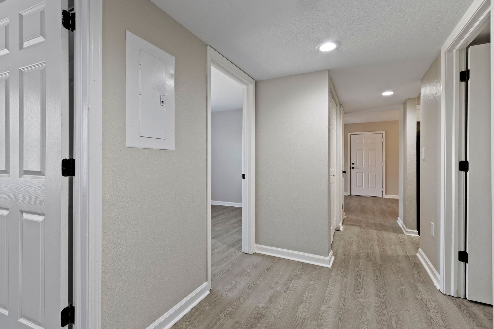 Hallway with light gray walls, wood-look flooring, white doors and trim, and recessed lighting.