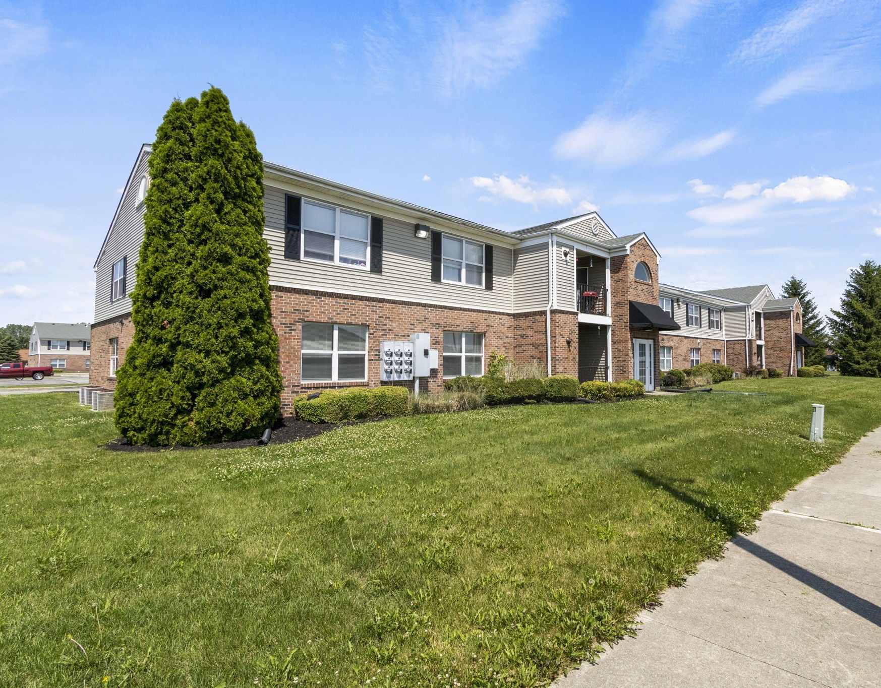 Two-story apartment building with brick and tan siding, a green lawn, and blue sky.