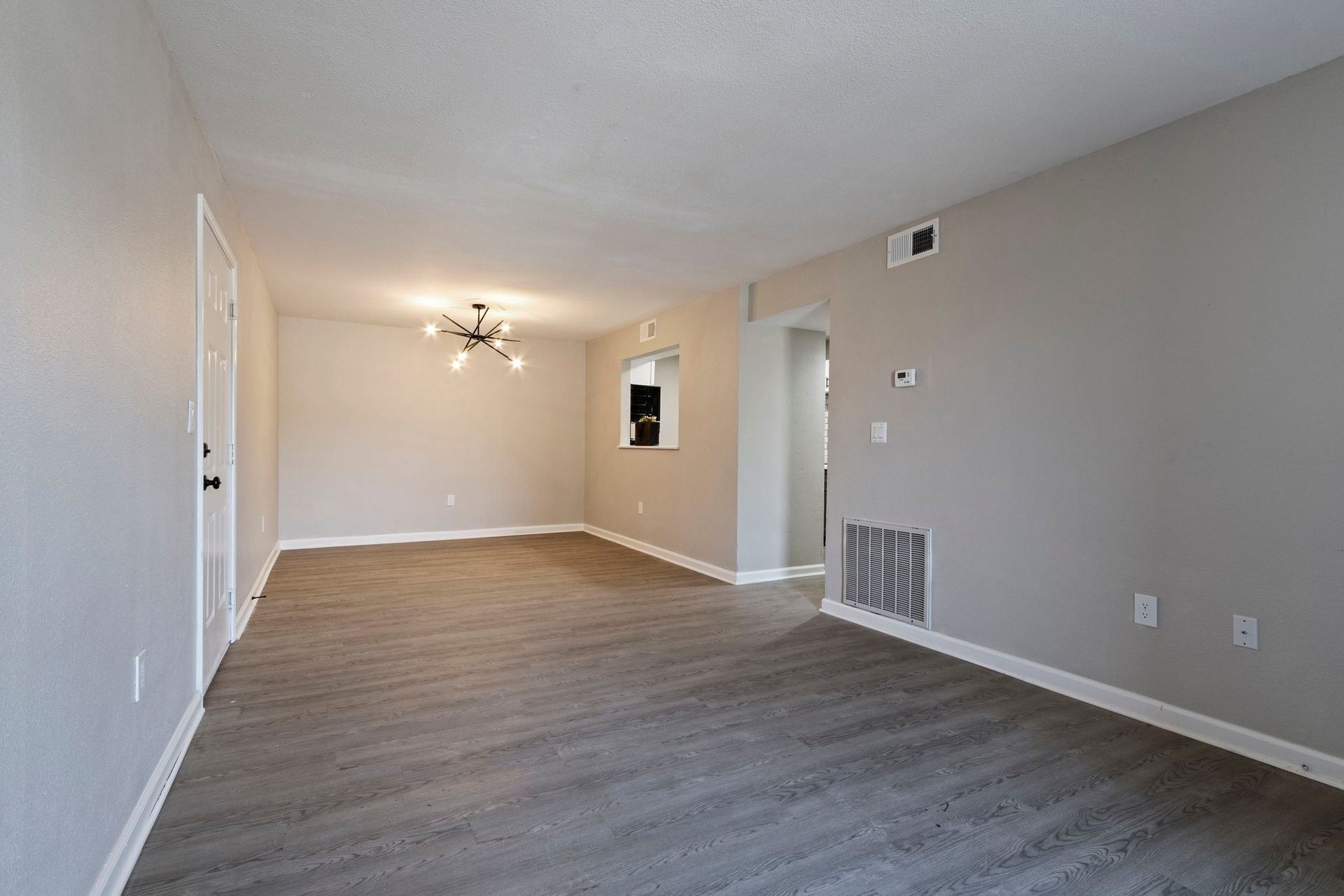 Empty living room with gray flooring and walls, chandelier, doorway, and vent.