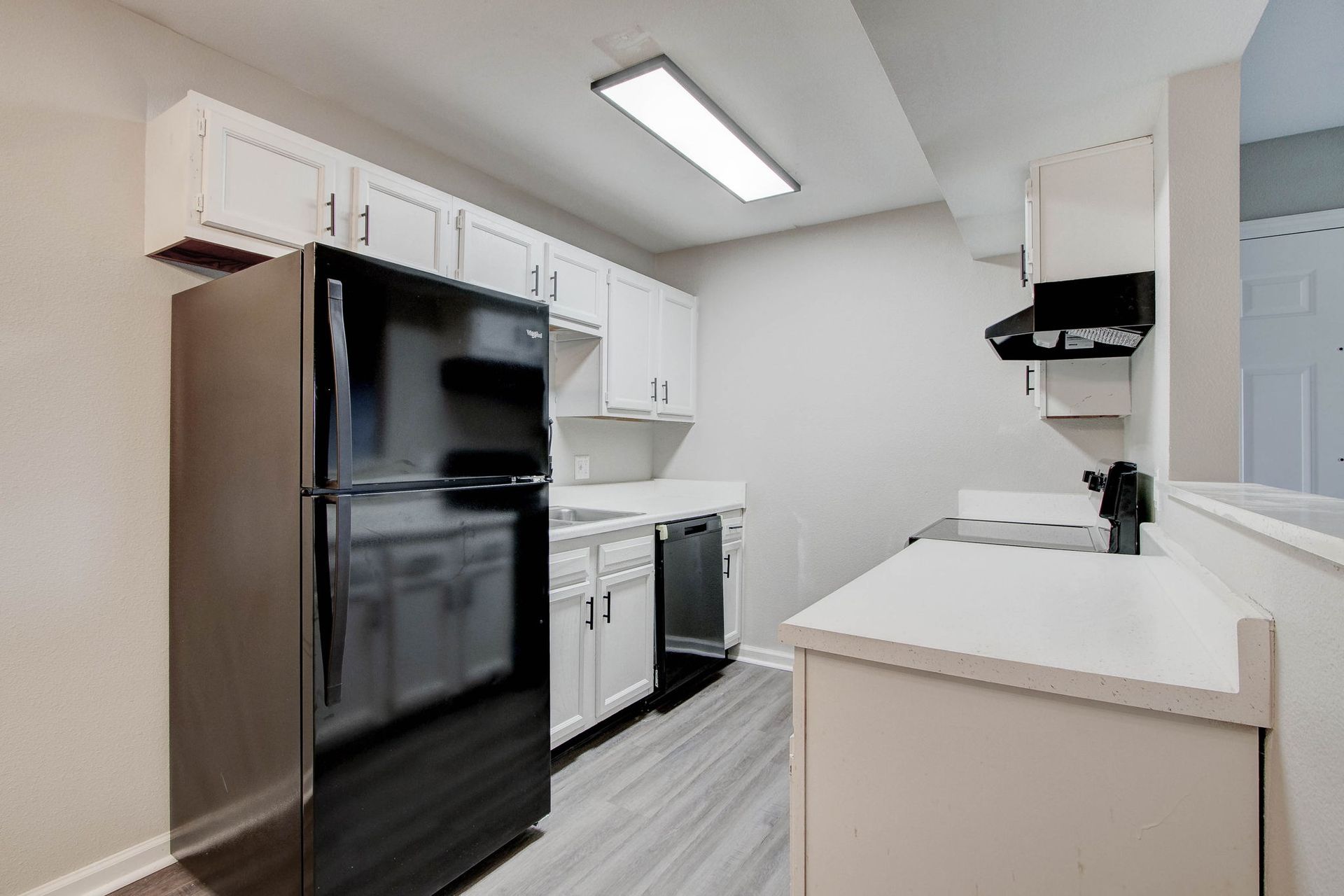 Black refrigerator and appliances in a white kitchen with overhead cabinets, grey floor, and white countertops.