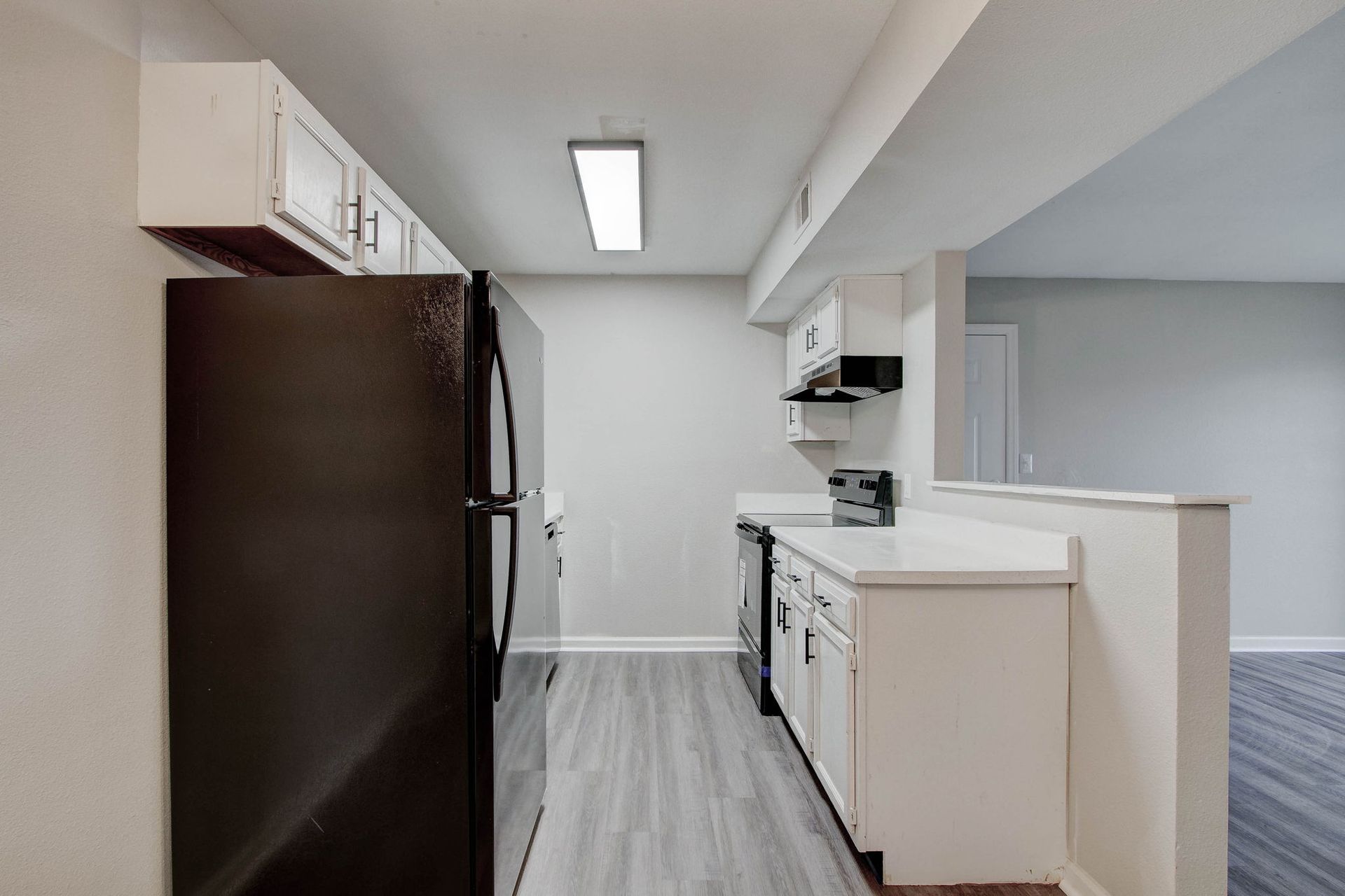 Kitchen with black refrigerator, white cabinets, light gray flooring, and a view into the living area.