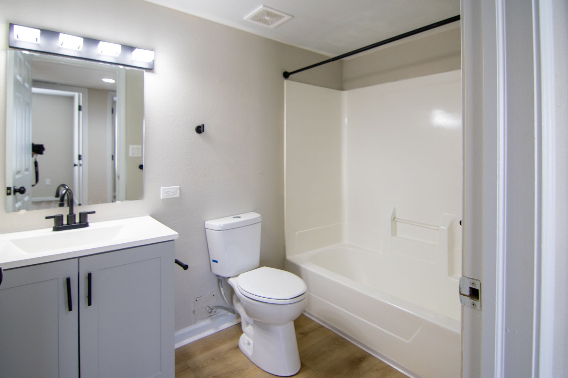 Bathroom with gray vanity, white toilet, and tub. Black fixtures on light walls, wood-look floor.