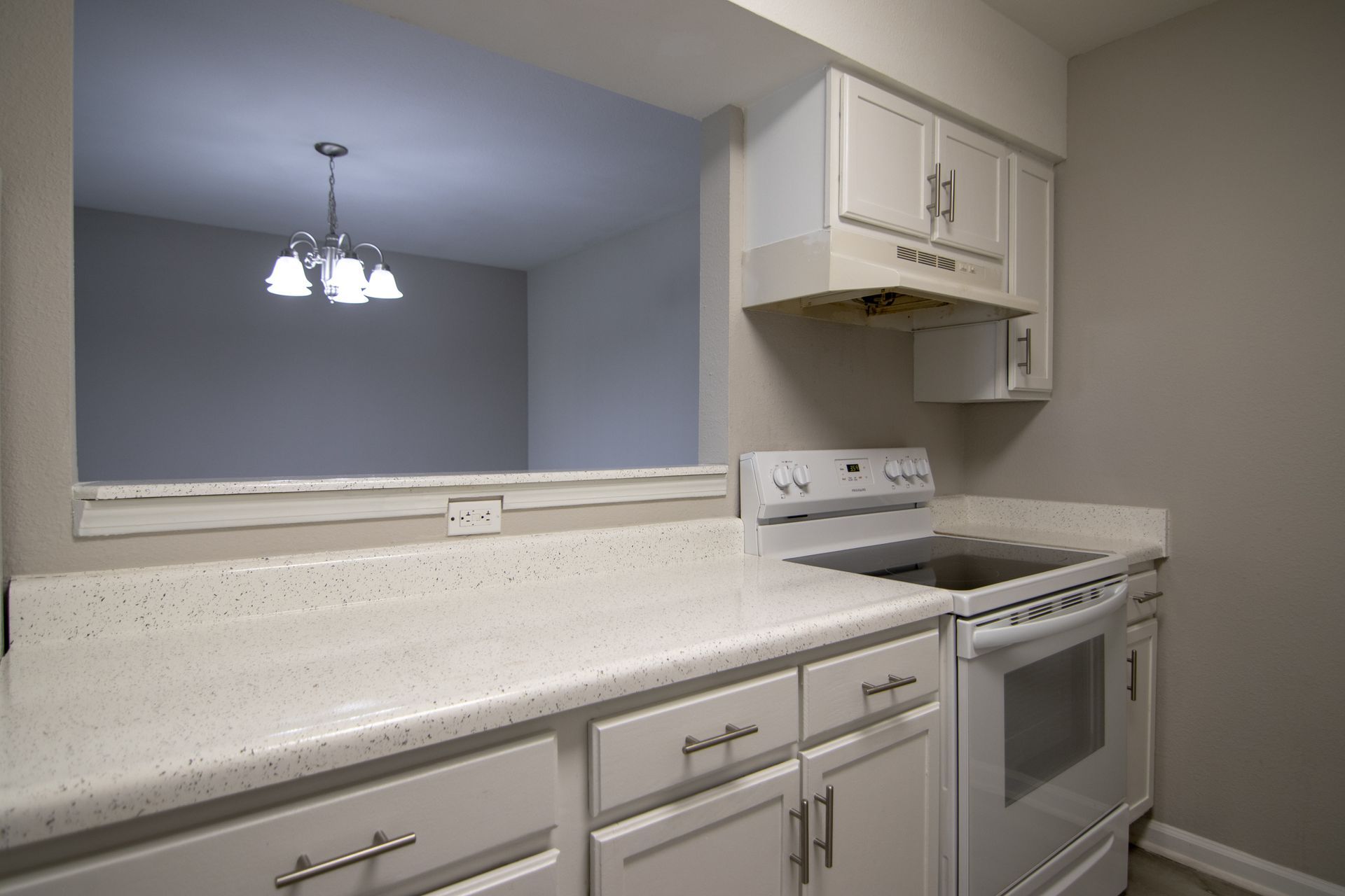 White kitchen with countertop, stove, cabinets, and pass-through to the dining area.