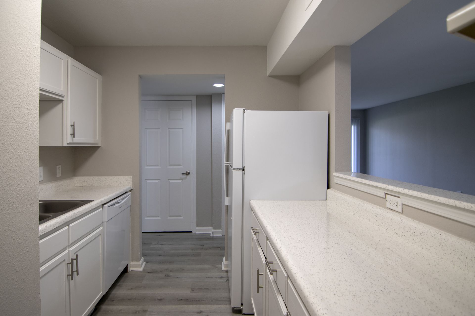 White kitchen with cabinets, refrigerator, and countertops; view towards a hallway.