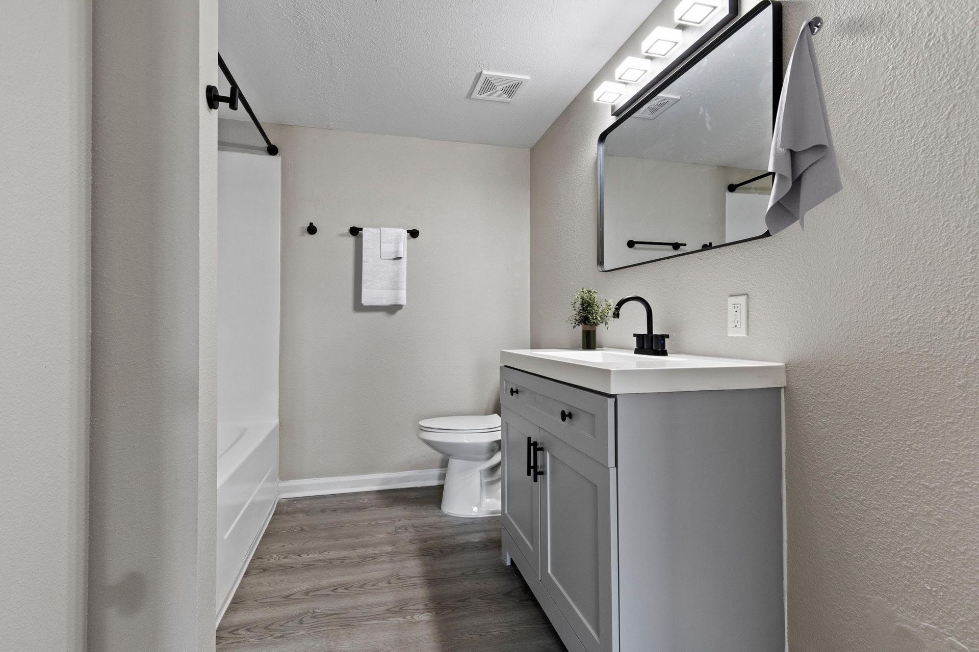 Bathroom with gray vanity, toilet, large mirror, and shower stall; neutral colors.