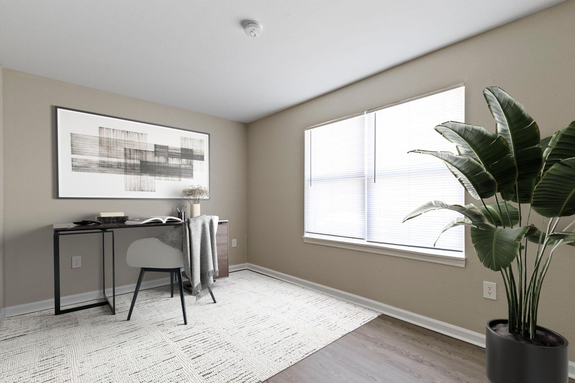 Office space with desk, chair, artwork, window, and potted plant. Beige walls and white rug.