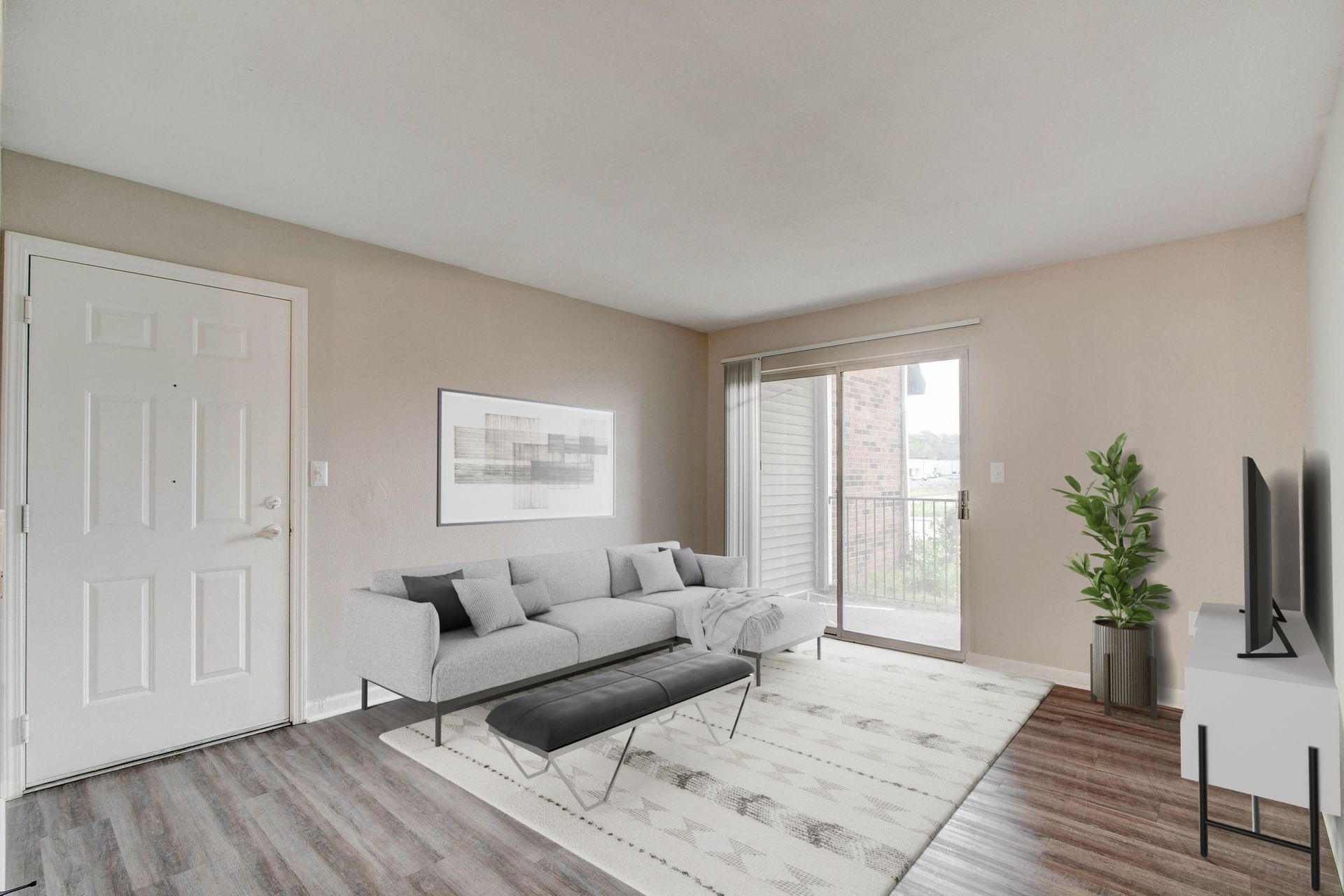 Living room with grey sofa, rug, door, balcony, and TV on a stand.