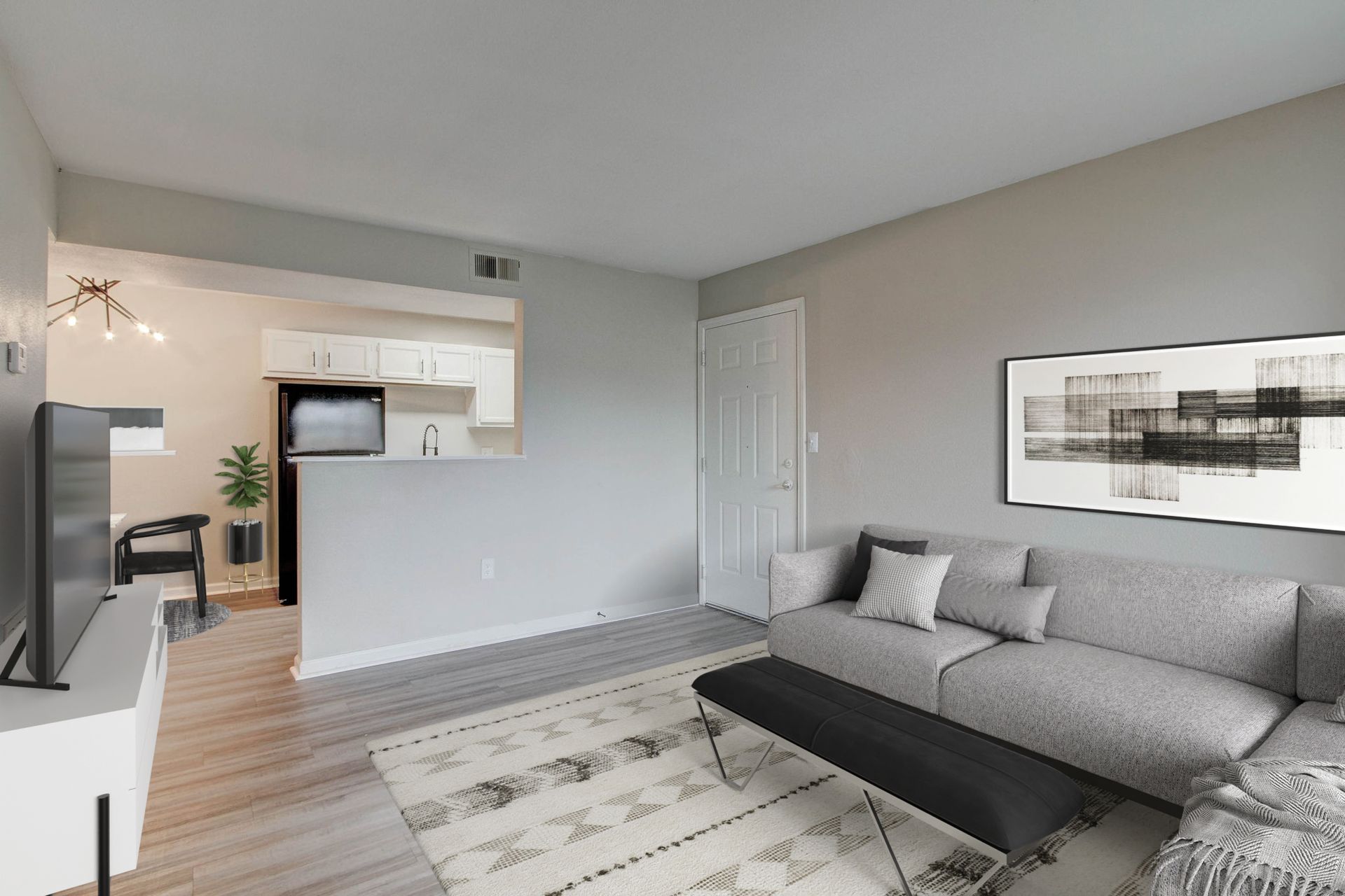 Living room with a gray sectional sofa, rug, and artwork; open to a kitchen.
