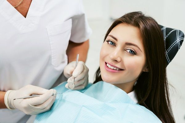 A woman is sitting in a dental chair while a dentist examines her teeth.