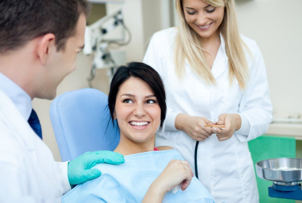 A woman is sitting in a dental chair talking to a dentist and a nurse.