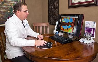 A dentist is sitting at a table looking at a computer screen.